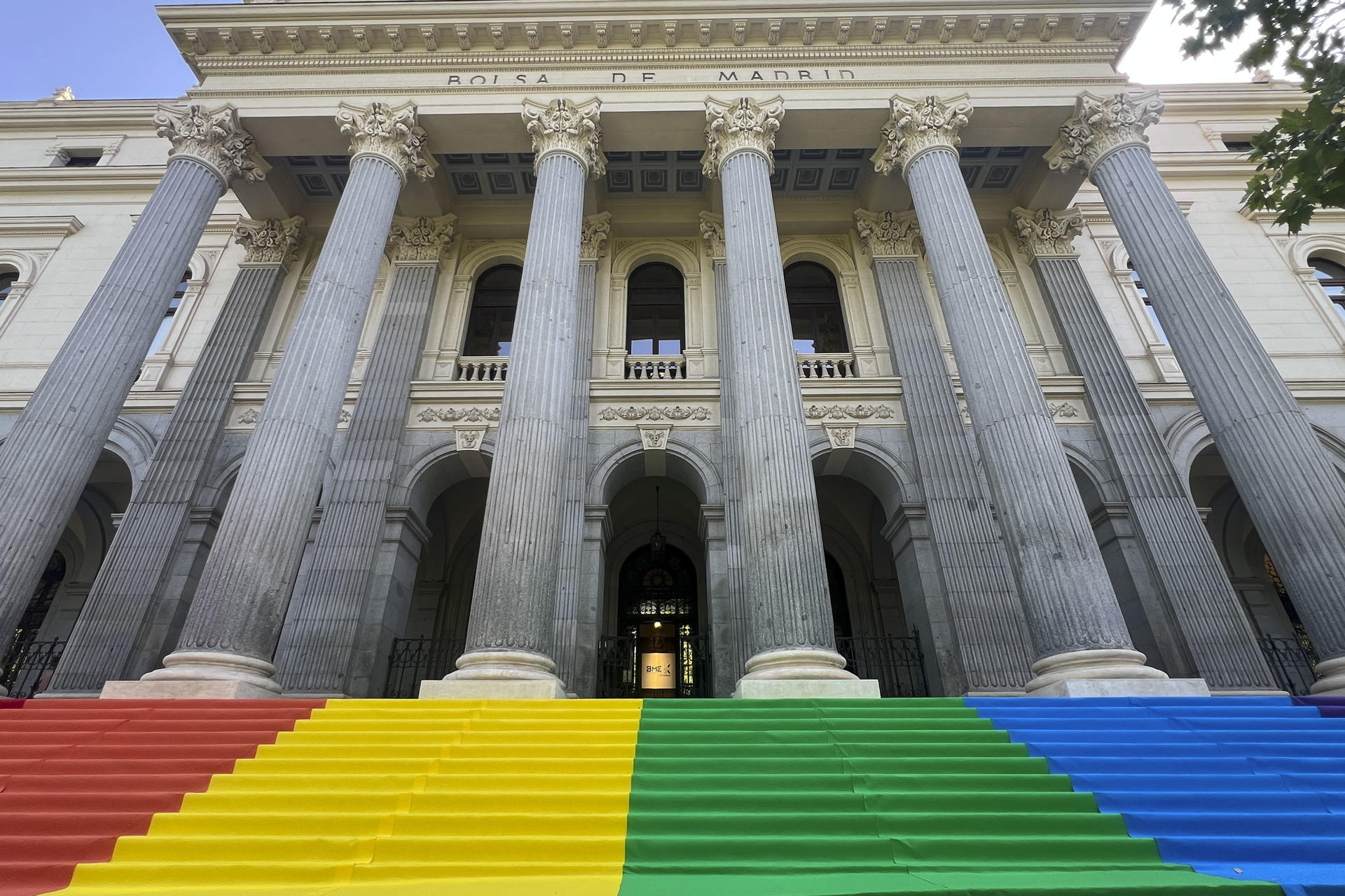El palacio de la Bolsa, en la plaza de la Lealtad de Madrid, ha desplegado este martes en su escalinata la bandera del Orgullo. EFE/ Altea Tejido Sánchez