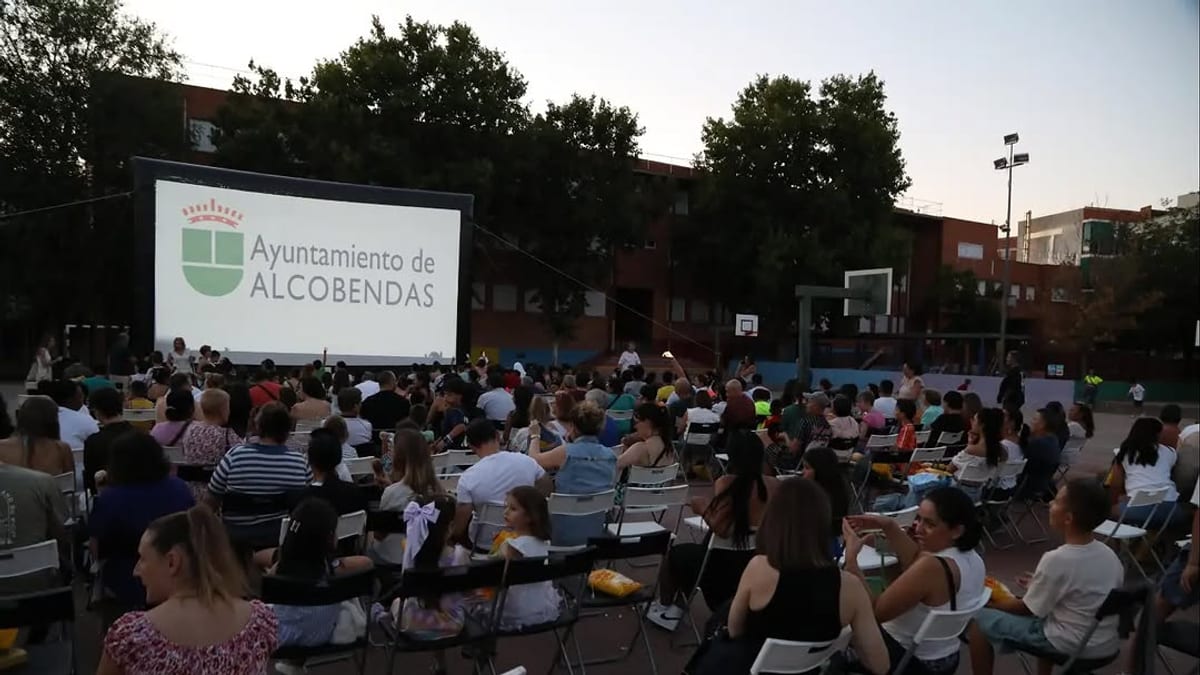 Familias disfrutando del Cine de Verano en la pista del CEIP Parque Cataluña de Alcobendas durante la proyección de 'Cómo entrenar a tu dragón'