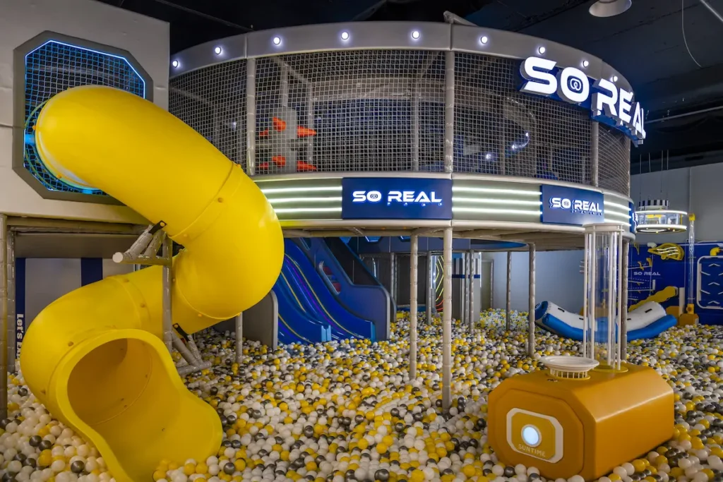 Parque infantil interior con tobogán amarillo en espiral, piscina de bolas y estructura de juego multinivel So Real.