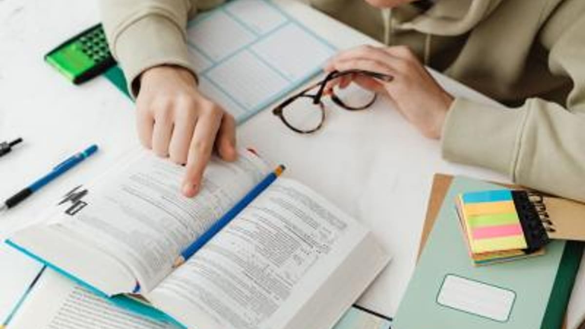 Estudiante con libros, cuadernos y materiales escolares en mesa de estudio