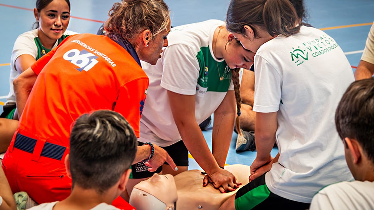 Participantes en un cardiomaratón 061 de formación en reanimación cardiopulmonar en Andalucía, con profesionales y voluntarios identificados con chalecos naranja.