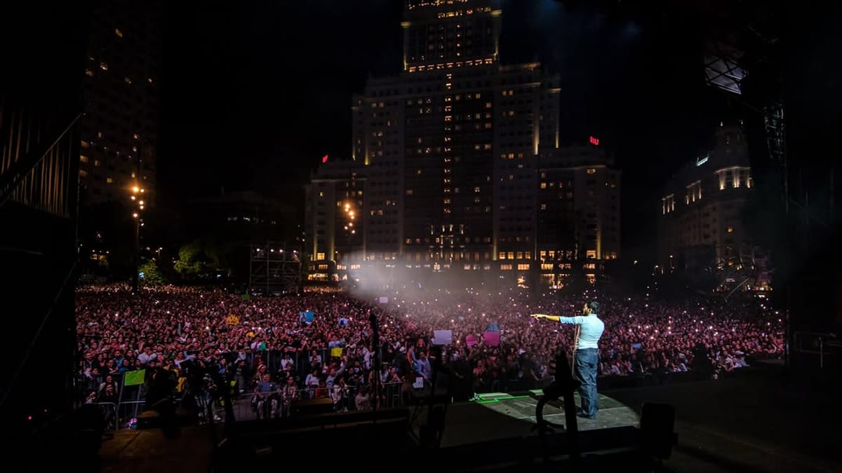 Multitud de personas en las calles de Madrid durante el concierto de Sebastián Yatra en el evento de Hispanidad Madrid, con edificios iluminados de fondo