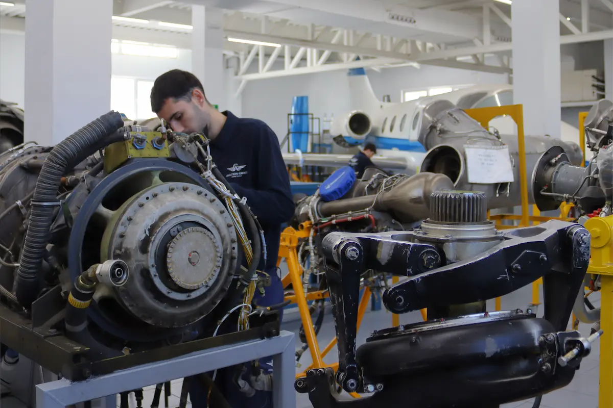 Técnico aeronáutico inspeccionando los componentes de un motor de avión en un taller de mantenimiento equipado.