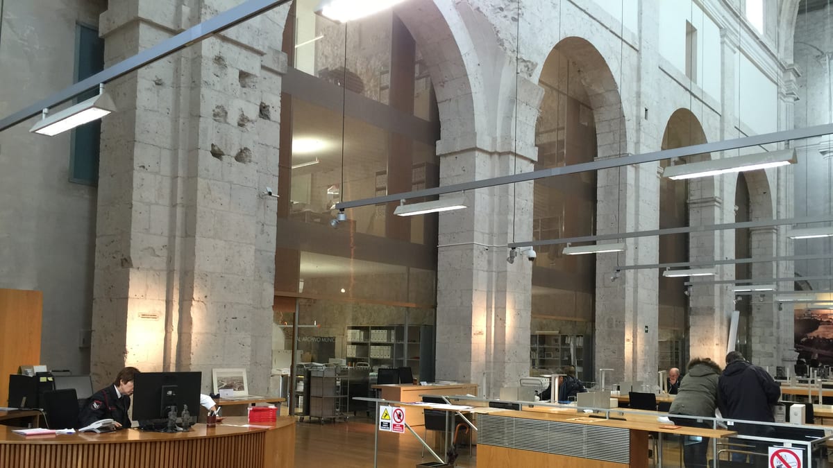 Interior de edificio institucional con arquitectura antigua de arcos de piedra y elementos modernos de iluminación