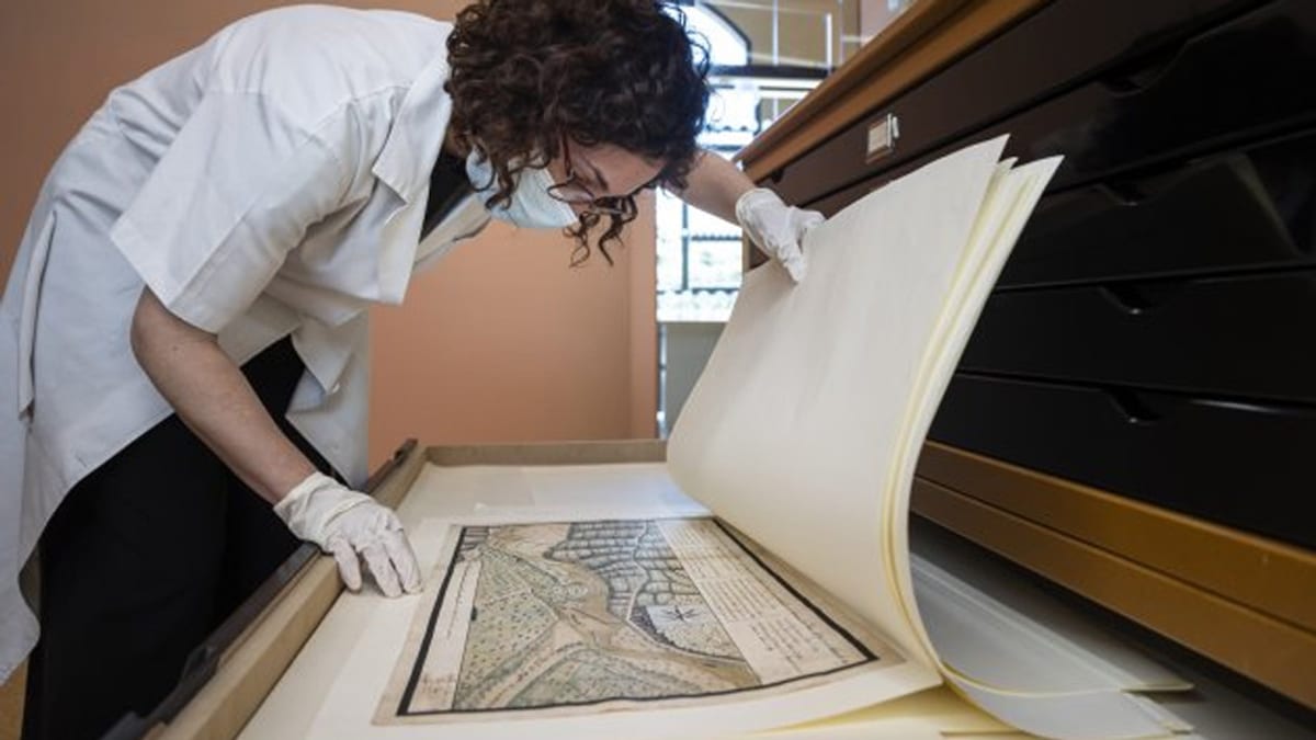 Persona examinant amb guants blancs un document o llibre històric antic amb mapes
