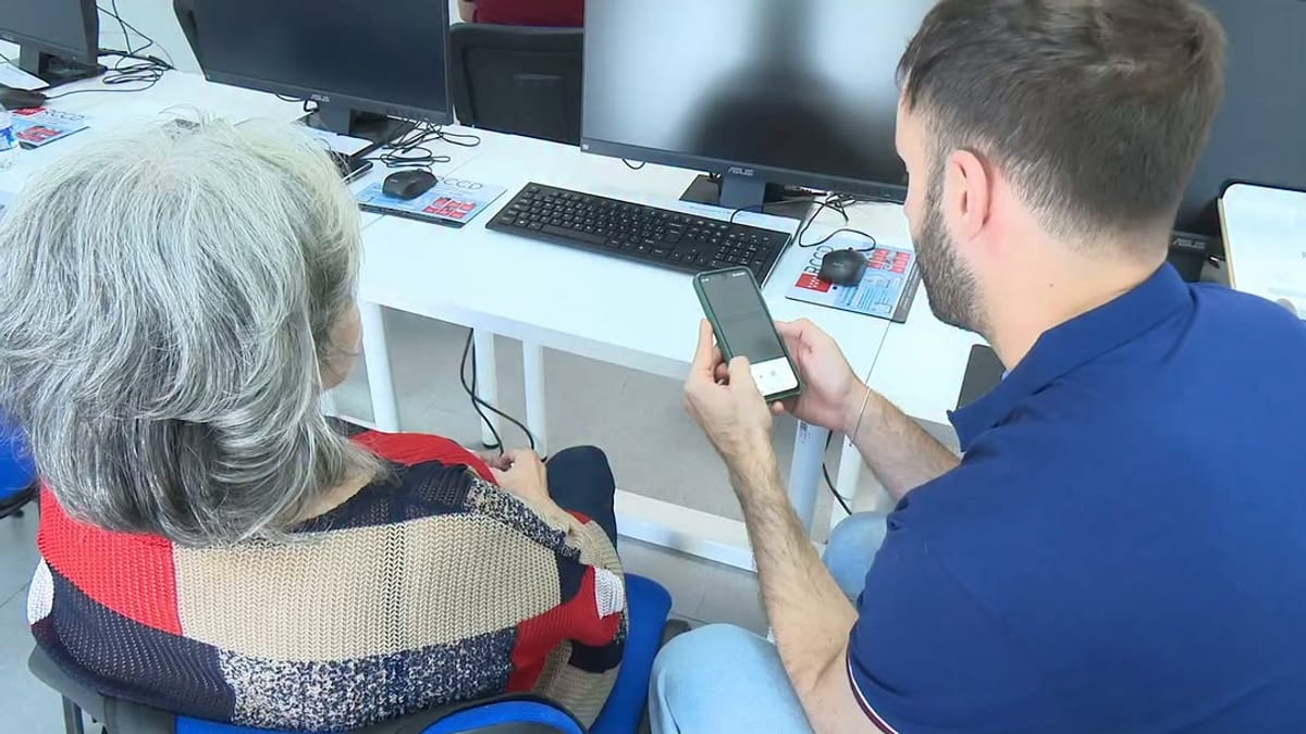 Dos personas trabajando en un escritorio con ordenador, teclado, monitor y teléfono móvil