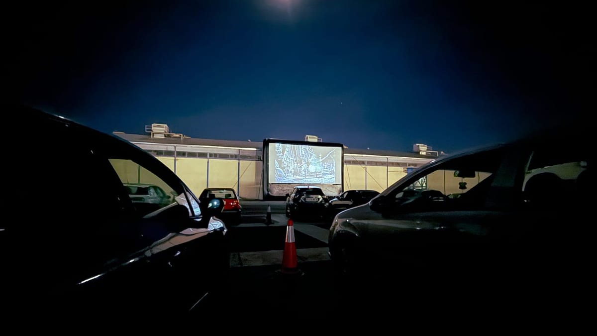 Autocine nocturno con automóviles estacionados frente a una pantalla de cine iluminada
