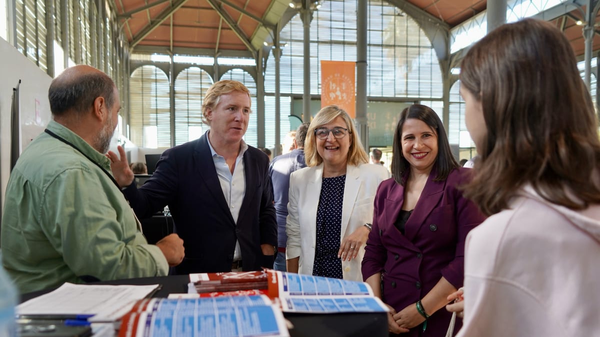 Grupo de personas en conversación durante la inauguración de la XV Feria Educativa de la UEx en Badajoz, con documentos sobre una mesa