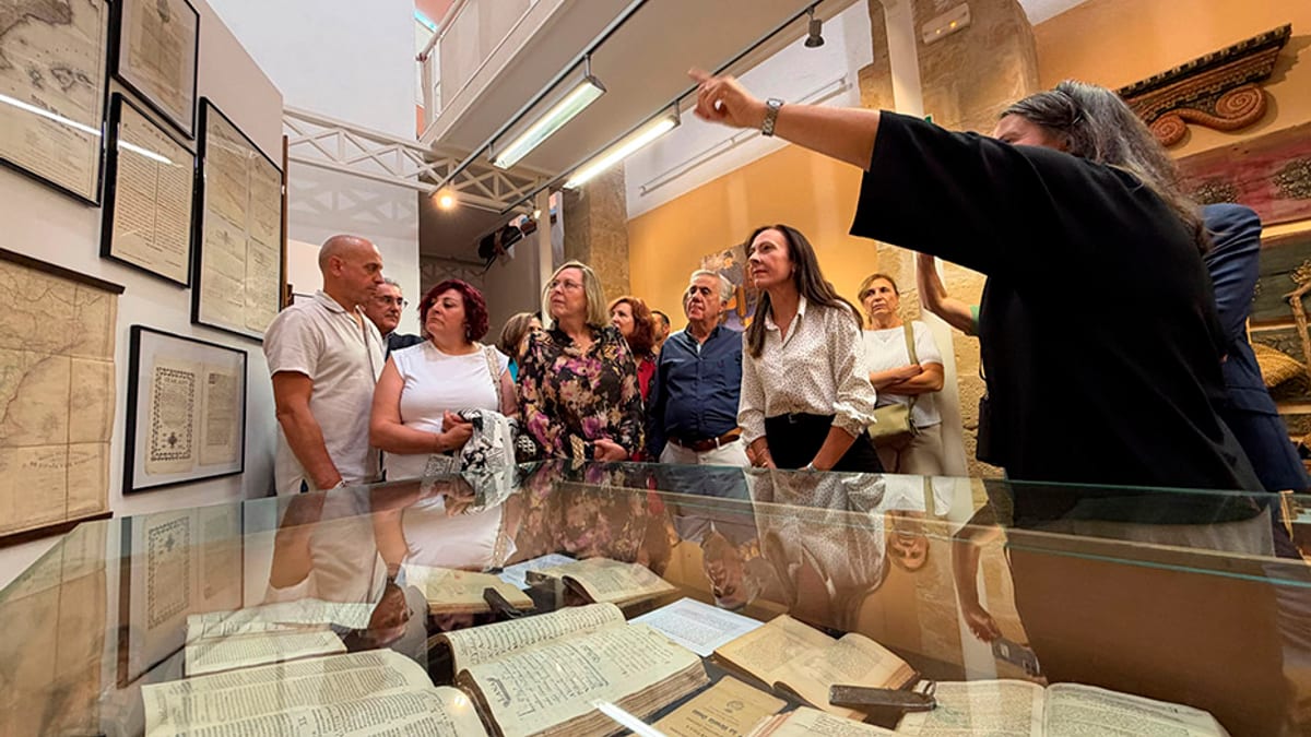 Grupo de visitantes en la exposición 'Cuidando la piel de la tierra' en Baeza, con documentos y mapas antiguos en vitrinas
