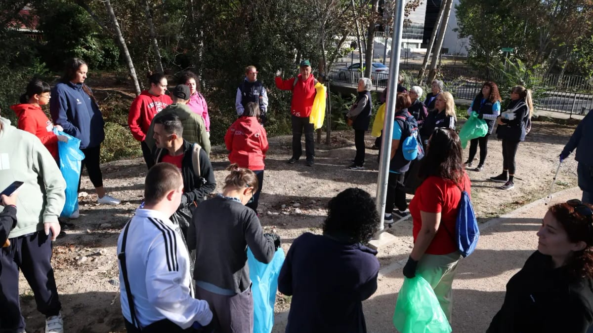 Grupo de participantes en la jornada Basuraleza en Familia sosteniendo bolsas de basura azul y verde durante la limpieza del arroyo de la Vega en Alcobendas