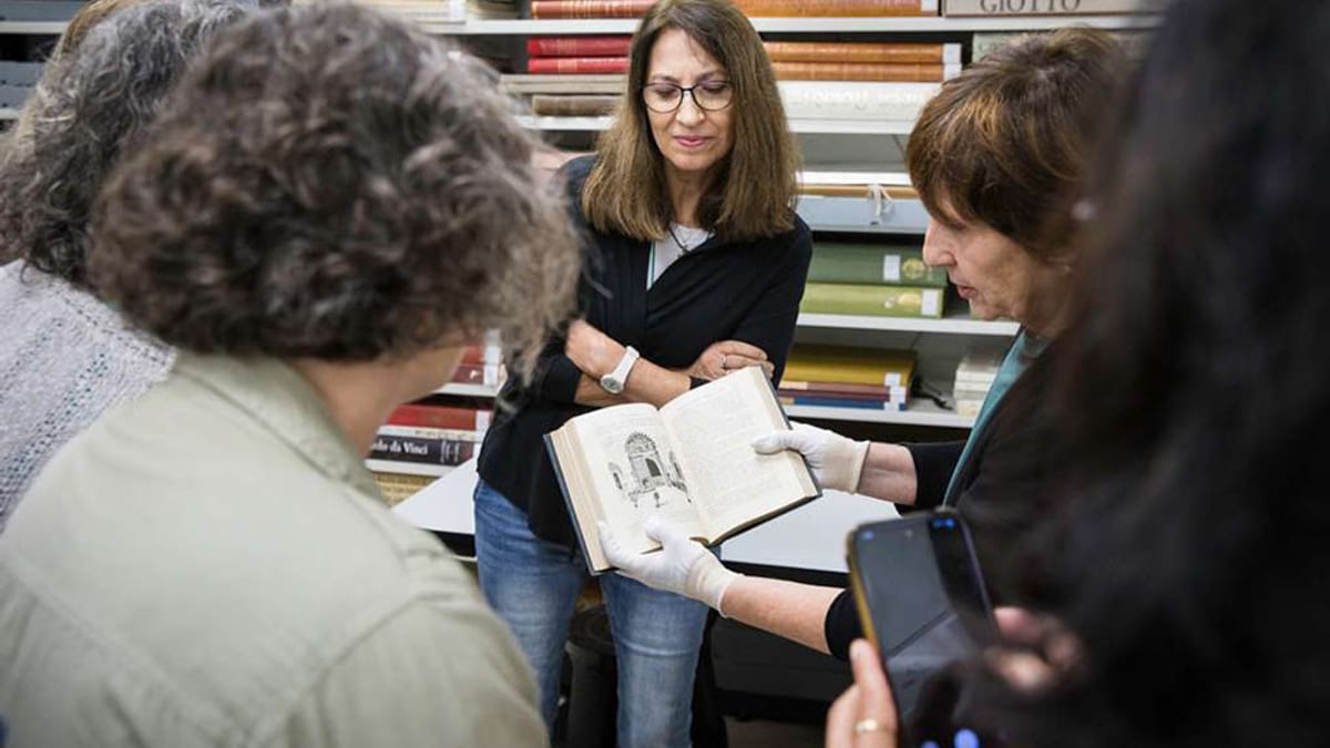 Personas en una biblioteca examina un libro abierto junto a estantes con libros de fondo