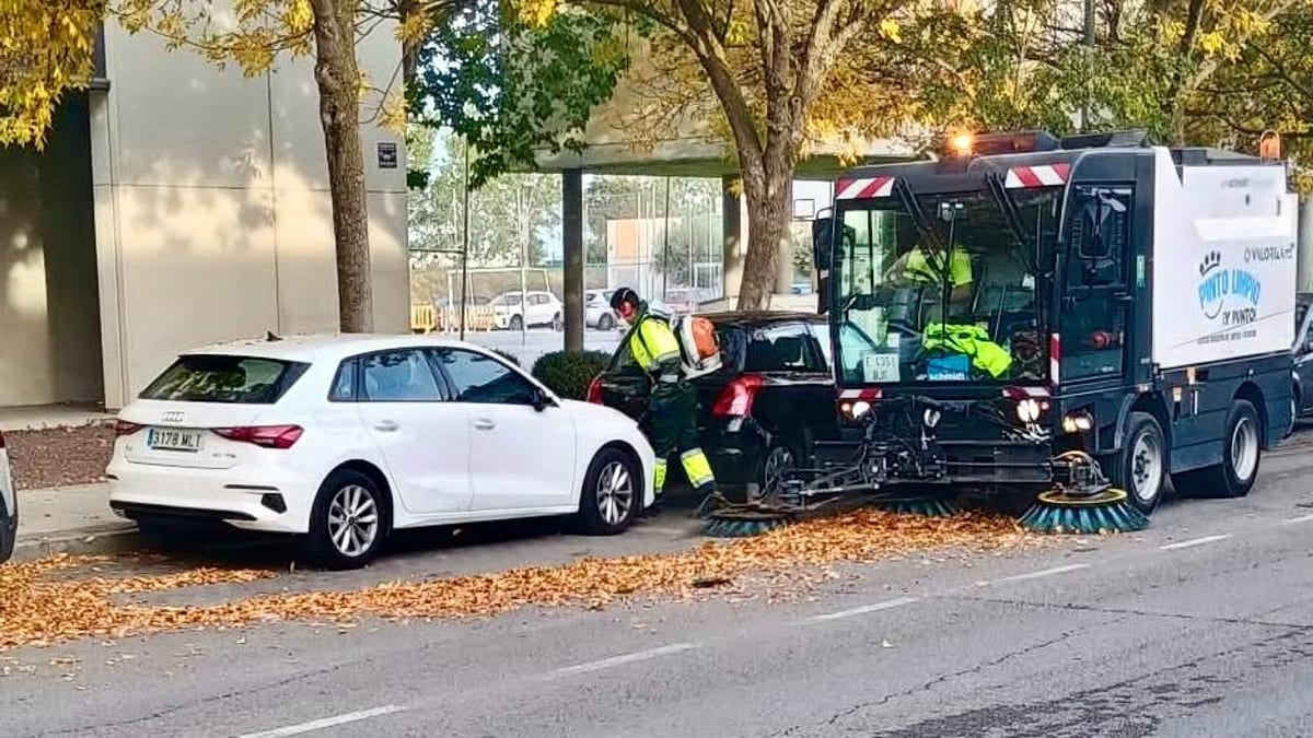 Máquina barredora municipal limpiando una calle de Pinto bajo árboles con follaje amarillo de otoño