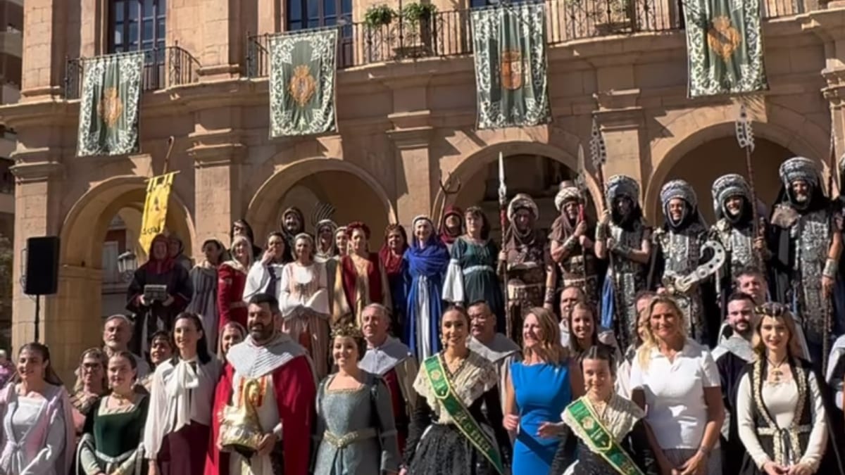 Acto de celebración del 9 de Octubre en Castellón con personas ataviadas con trajes tradicionales medievales en la plaza frontal de un edificio histórico neoclásico con banderas españolas