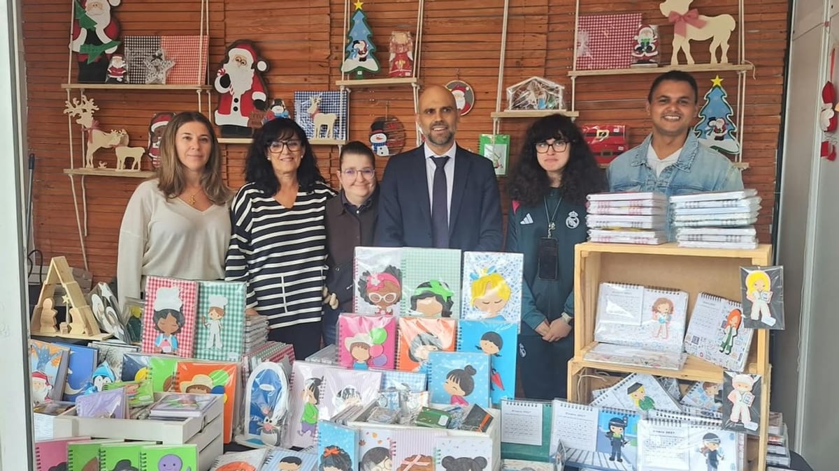 Grupo de personas en el stand del Centro Ocupacional Valenzana de Illescas en FARCAMA Toledo, con trabajos escolares y decoraciones navideñas de fondo