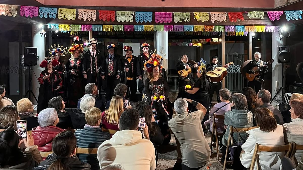 Concierto musical en vivo con decoraciones de papel picado y músicos en traje tradicional mexicano ante una audiencia