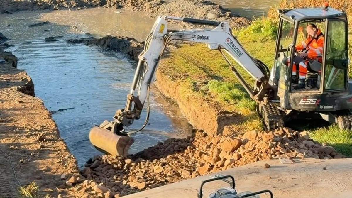 Trabajos de construcción de la nueva rampa de acceso al embarcadero del río Ebro en Logroño, con maquinaria Bobcat en la margen izquierda