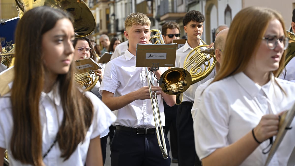 Jóvenes músicos en uniforme blanco tocando instrumentos de viento en un desfile callejero