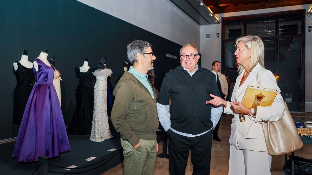 Visitantes observan maniquíes con vestidos elegantes en la inauguración de la exposición 'La edad dorada de la moda española' en la Sala de la Pasión