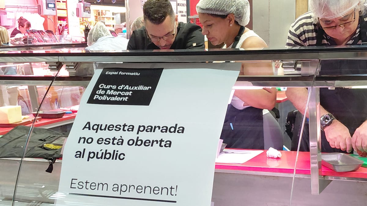 Parada de mercat amb cartell informatiu sobre el Curs d'Auxiliar de Mercat Polivalent de l'Escola d'Oficis dels Mercats Municipals