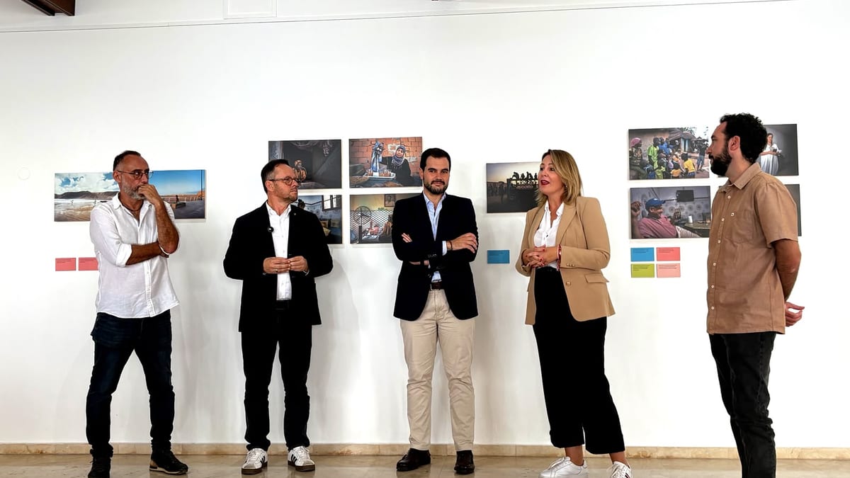 Grupo de personas de pie frente a la exposición Travesías en Puerto de la Cruz con fotografías y elementos visuales en una pared blanca