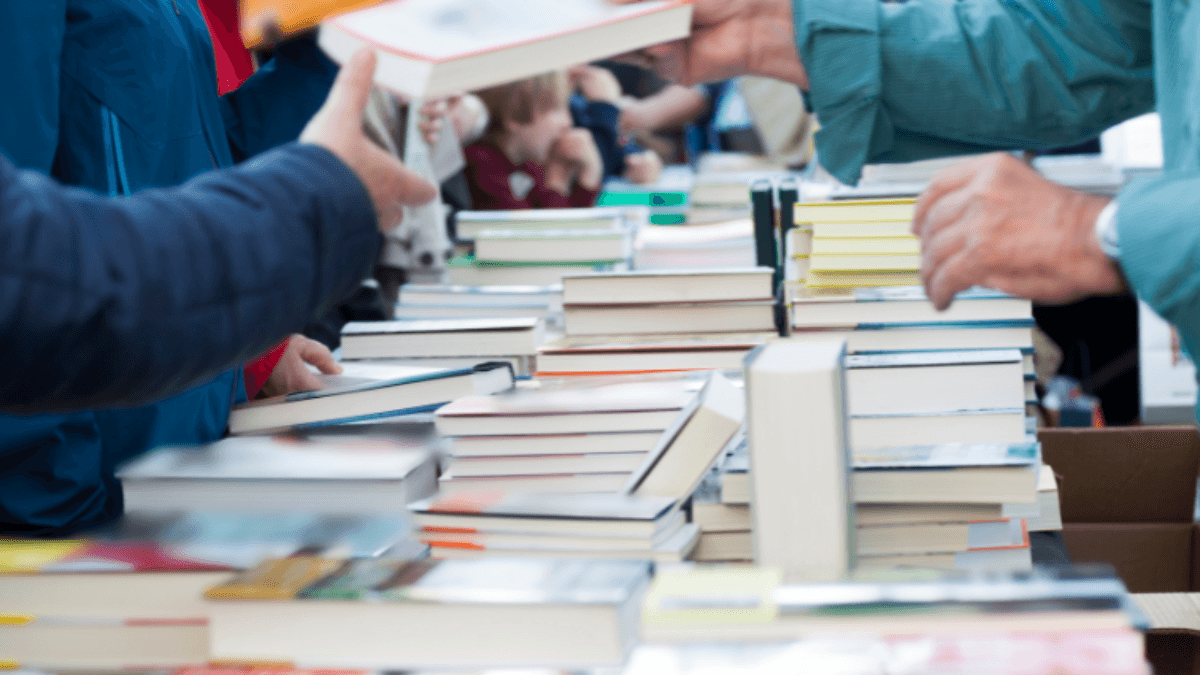Visitantes interactuando con pilas de libros en una feria literaria