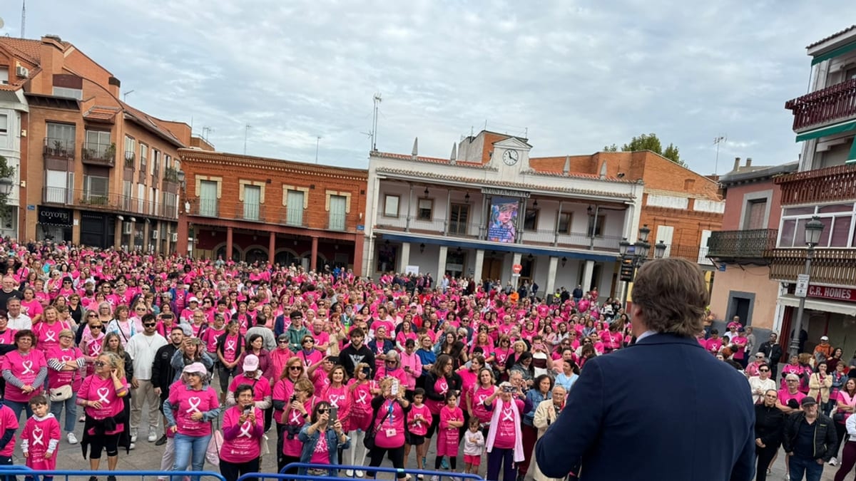 Concentración masiva de ciudadanos vistiendo camisetas rosa en una plaza de Fuenlabrada contra el cáncer de mama, con orador dirigiéndose a la multitud