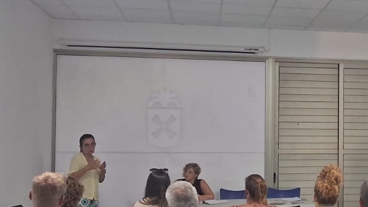 Sala de encuentro comunitario con asistentes sentados escuchando una presentadora durante el inicio del proyecto Fuerteventura Protagonista