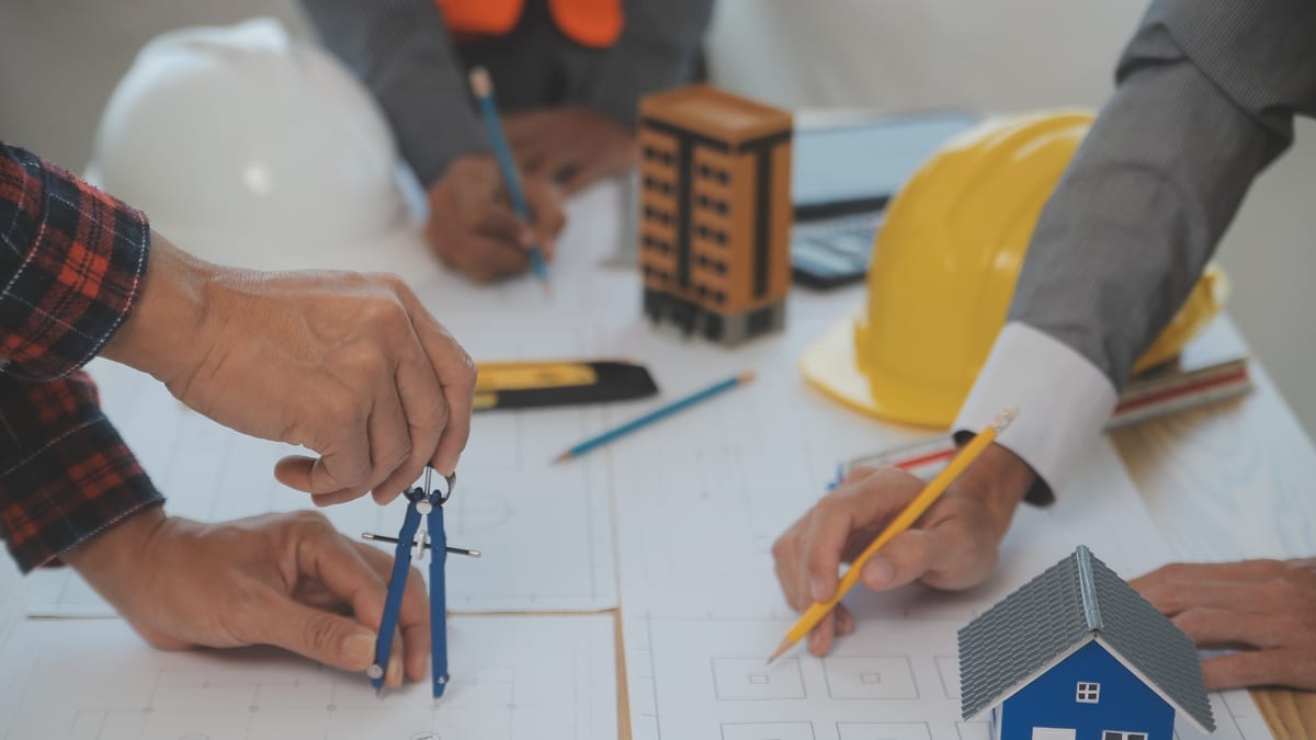 Maqueta de vivienda, planos de construcción y cascos de seguridad sobre mesa de trabajo colaborativo en proyecto de edificación