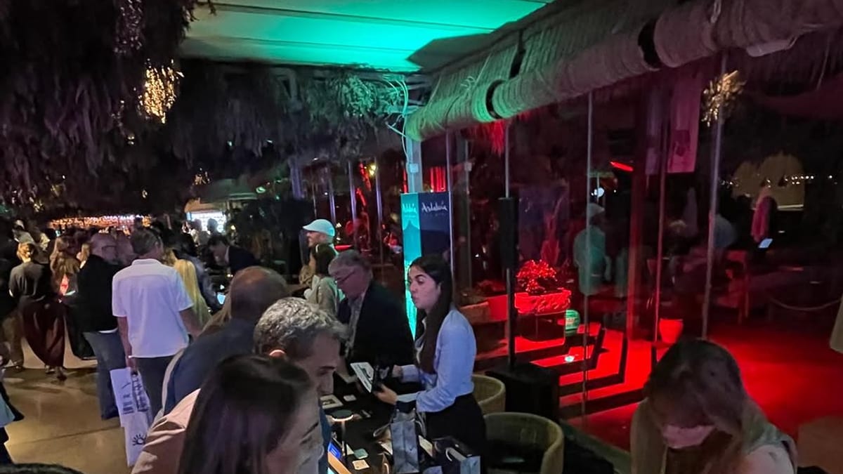 Evento de las Jornadas de Andalucía en Levante con iluminación de neón, asistentes y puestos de atención de la Diputación de Huelva promocionando Destino Huelva