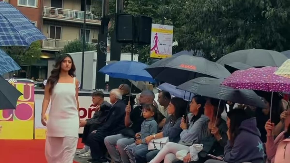 Modelo desfilando en la pasarela de la II Gala CUCO de la Moda Riojana bajo la lluvia, con público con paraguas en el Parque Gallarza de Logroño