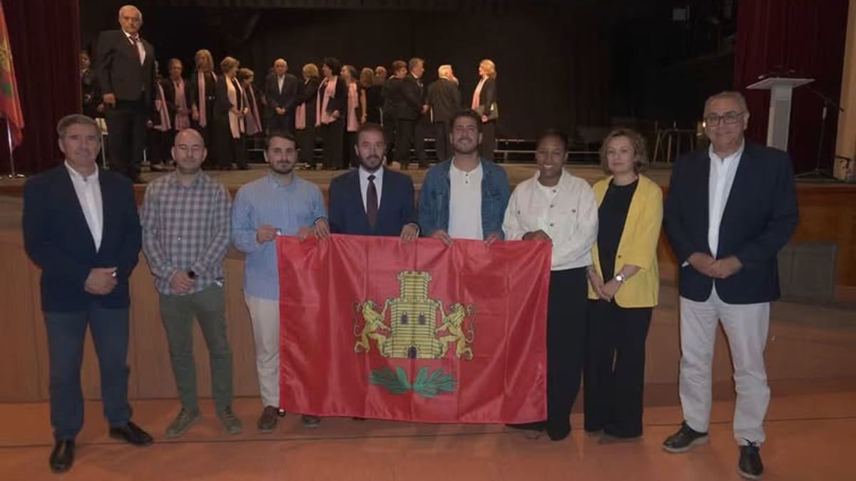 Grupo de representantes institucionales posan con la nueva bandera municipal de Iniesta, que luce un escudo rojo en el centro, durante la presentación en el Auditorio Municipal