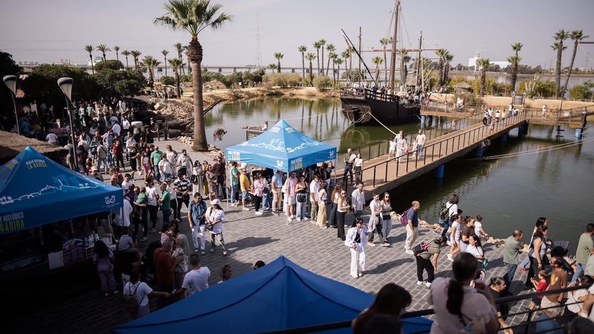 Escena del evento en La Rábida con carpas azules, visitantes, palmeras y barcos históricos en el muelle