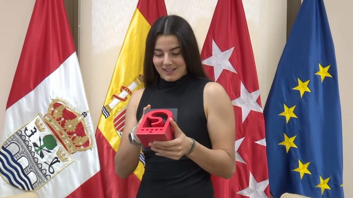 Laia López de la Morena, portera del Real Madrid, sostiene un objeto rojo frente a banderas de España, Madrid y la Unión Europea en el Ayuntamiento de San Sebastián de los Reyes