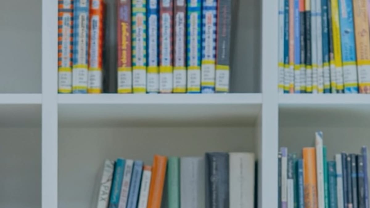 Estantería blanca con libros organizados por series y colores en la biblioteca de Castellón
