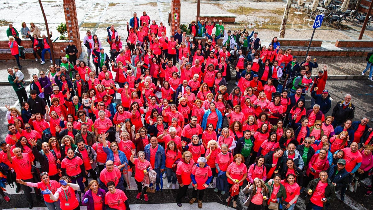 Fotografía aérea de un gran grupo de personas reunidas en el espacio público vistiendo camisetas rojas durante la marcha solidaria contra el cáncer de mama en Torrijos