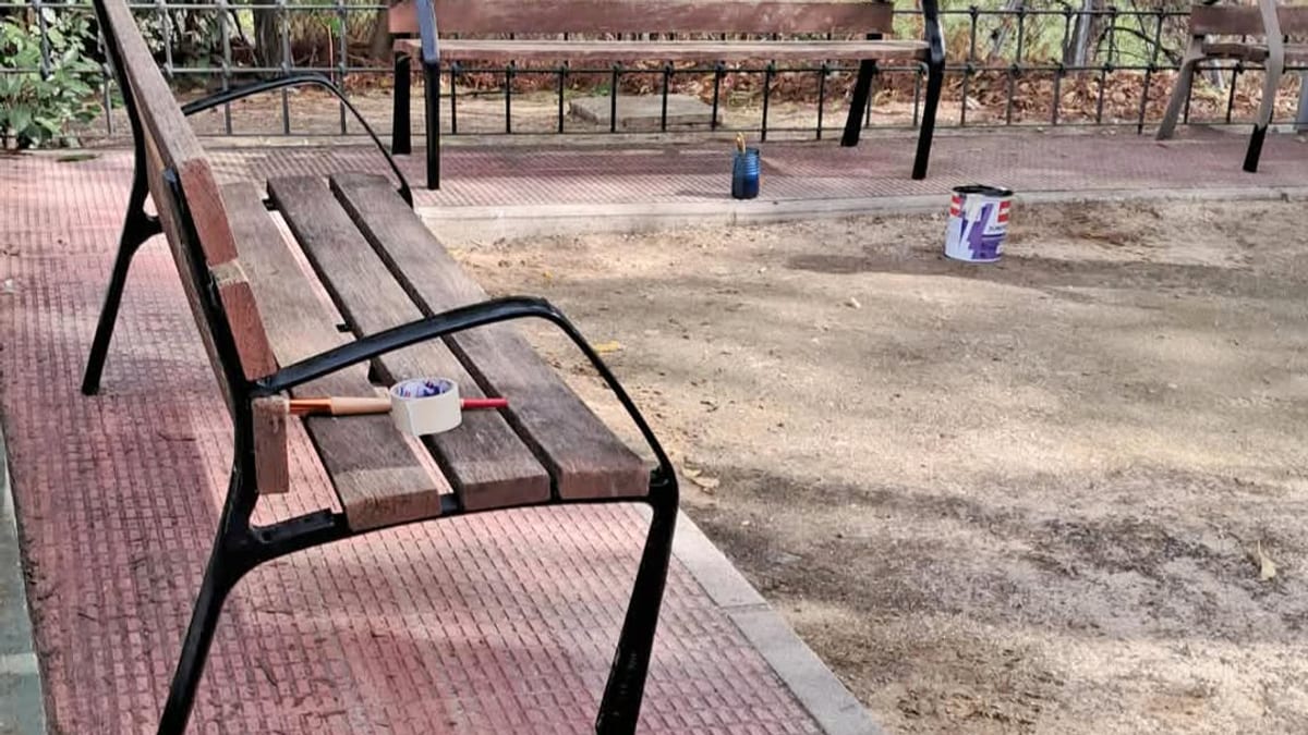 Trabajos de mantenimiento en un área infantil de Paracuellos de Jarama con bancos, herramientas de pintura y materiales de construcción