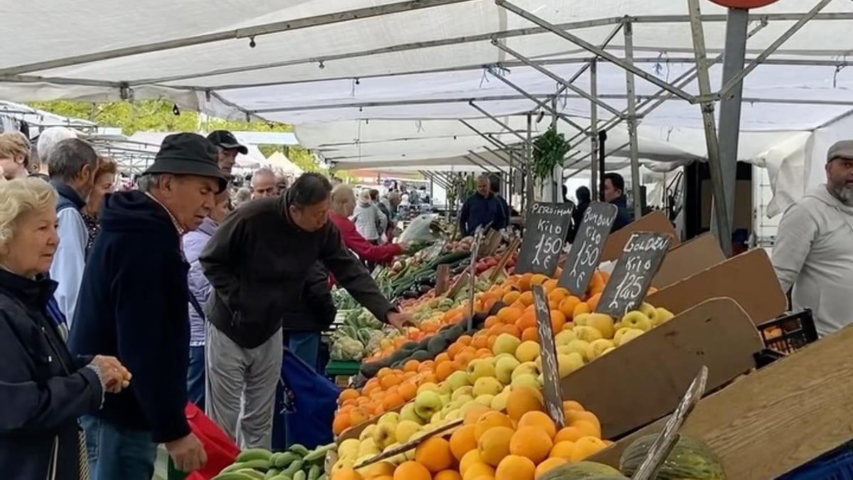 Puesto de frutas y verduras del Mercadillo Municipal de Alcobendas con diversos productos y clientes comprando