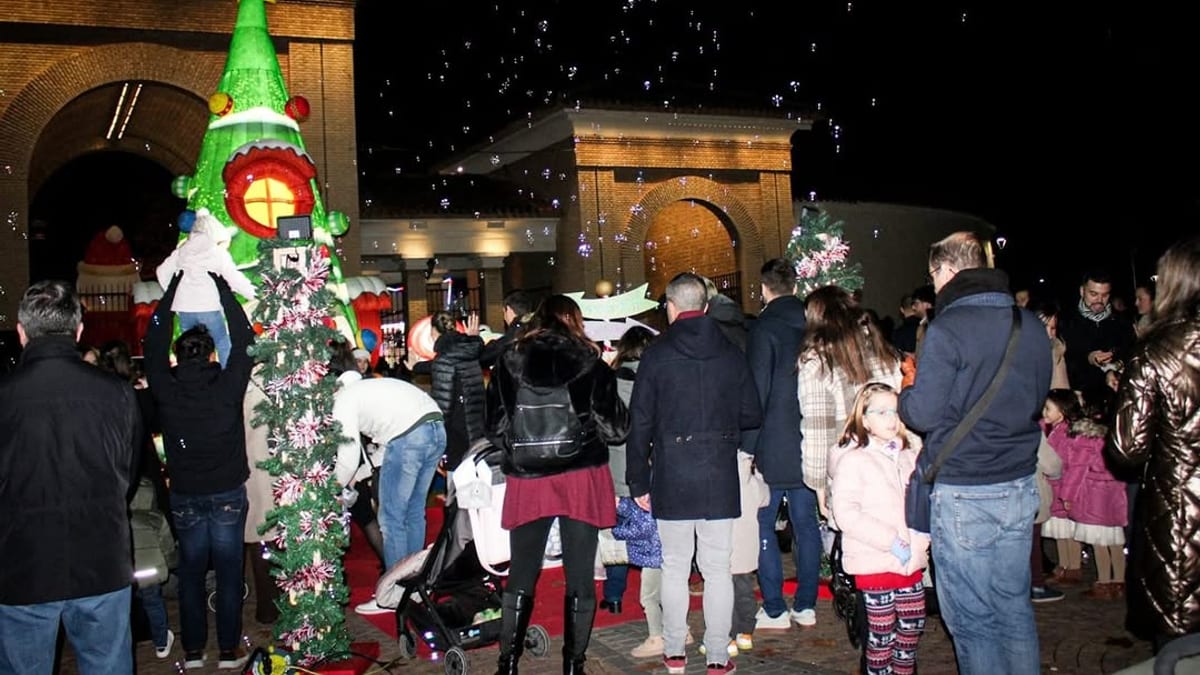 Escena nocturna de Navidad en la Feria con árbol de Navidad iluminado, personas disfrutando y edificios navideños de fondo en Albacete