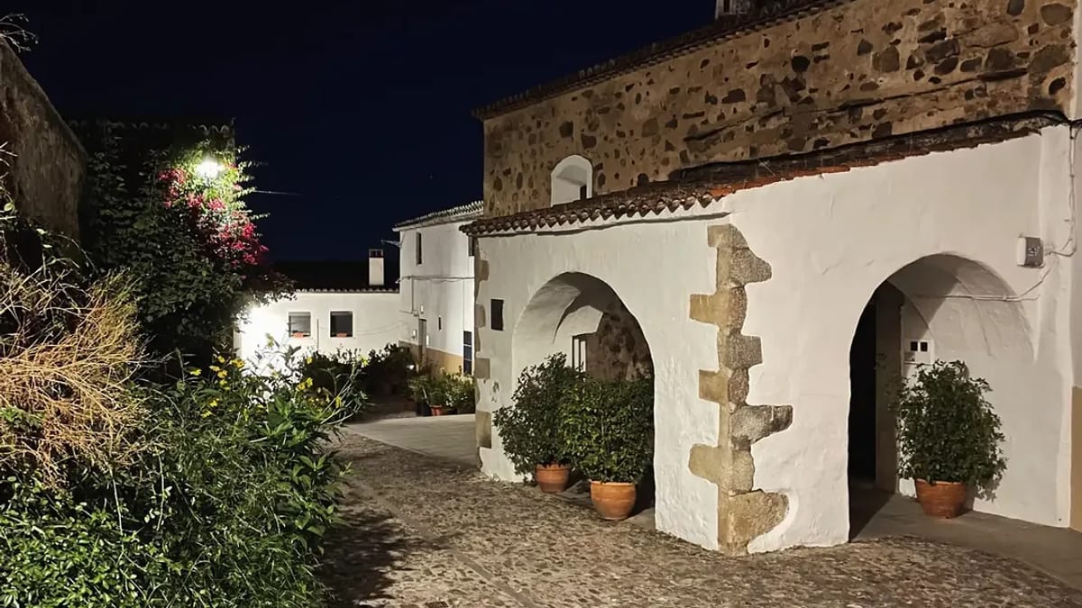 Callejuela nocturna de la Judería Vieja de Cáceres con adoquines de piedra y muros históricos iluminados, mostrando la arquitectura medieval del patrimonio sefardí