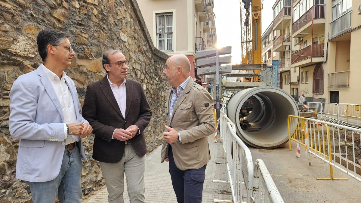 Responsables municipales durante la visita a las obras de renovación de redes de agua en Camino Llano, Cáceres, con tuberías de hormigón y edificios históricos al fondo