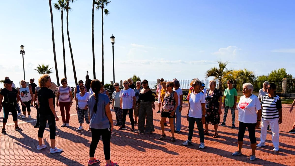 Grupo de personas mayores reunidas en una plaza junto al paseo marítimo de Torremolinos con palmeras al fondo