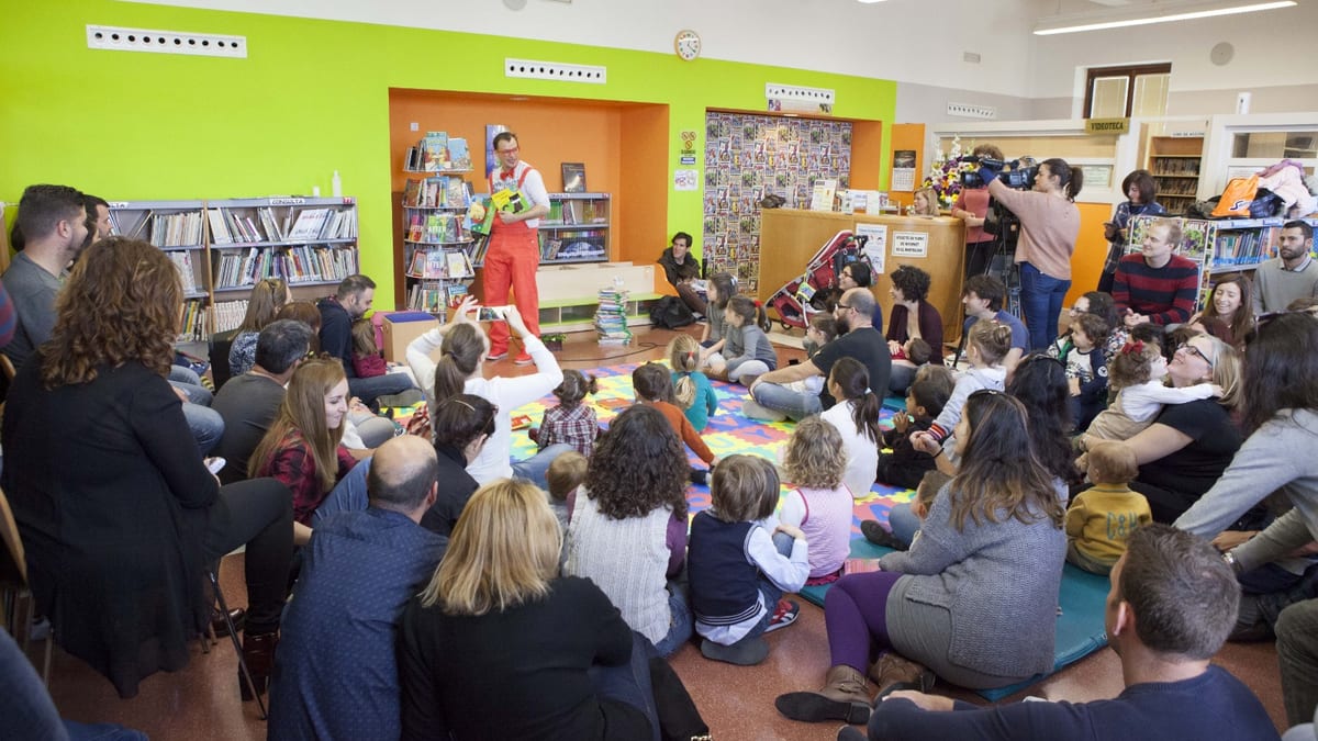 Actividad de biblioteca infantil con performer en ropa roja actuando ante audiencia de niños y adultos sentados