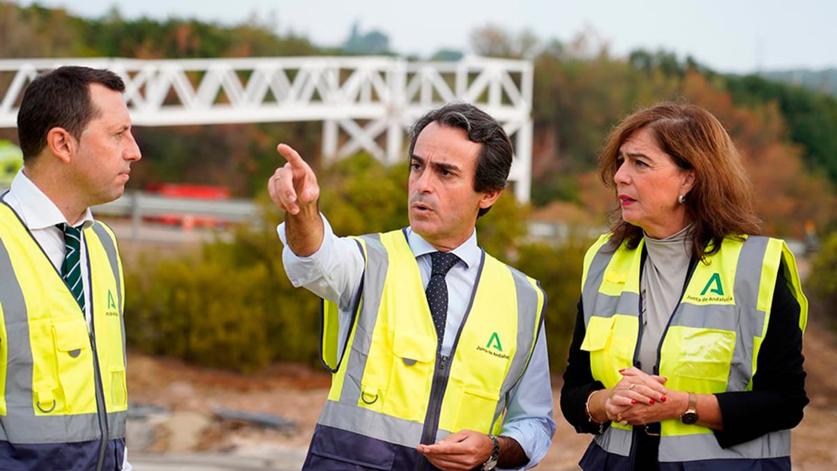 Trabajadores en chaleco de seguridad durante los trabajos de instalación de la pasarela peatonal de Palma del Río, con estructura metálica de puente al fondo