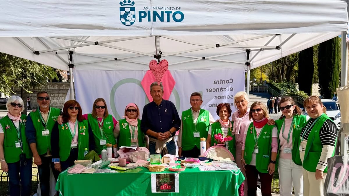 Mesa informativa sobre cáncer de mama organizada por la Asociación Española contra el Cáncer en Pinto, con presencia de vecinos y autoridades municipales