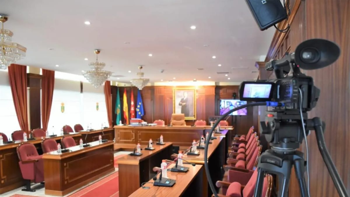 Sala de sesiones del Ayuntamiento de Villaviciosa de Odón con mobiliario de madera, sillas rojas y cámara de video