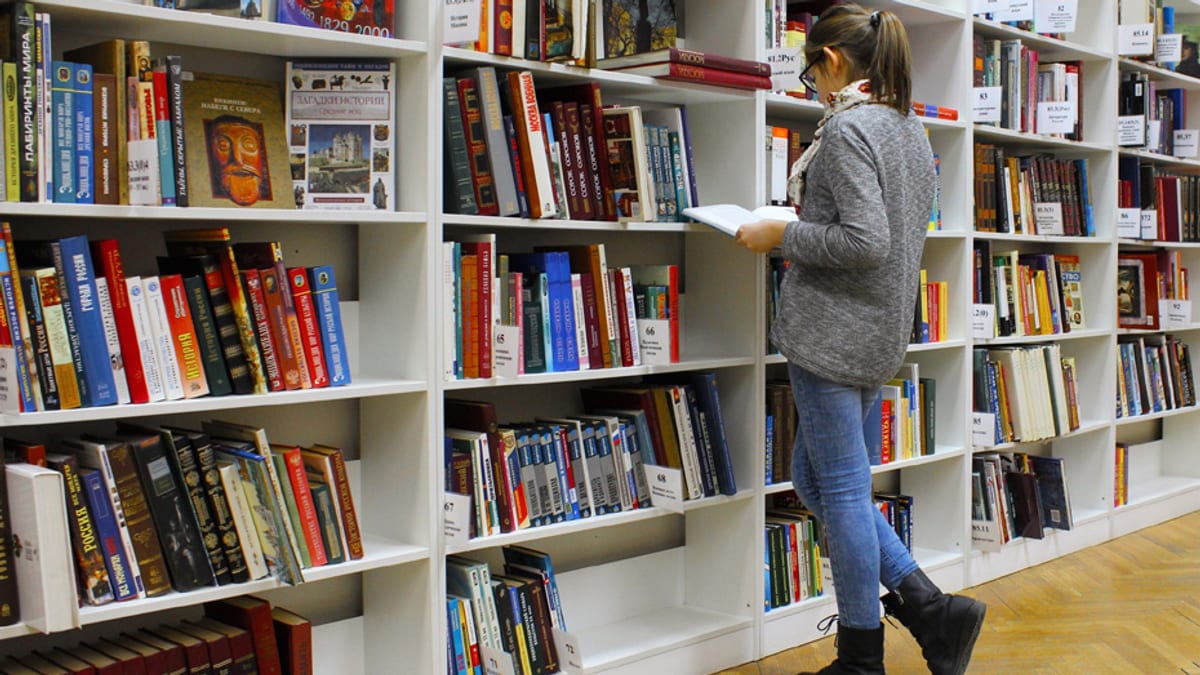 Persona consultando libros en una biblioteca escolar con estanterías blancas