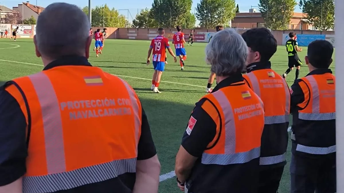 Miembros de Protección Civil de Rivas Vaciamadrid con chalecos reflectantes observando el partido de fútbol entre CD Navalcarnero y Atlético