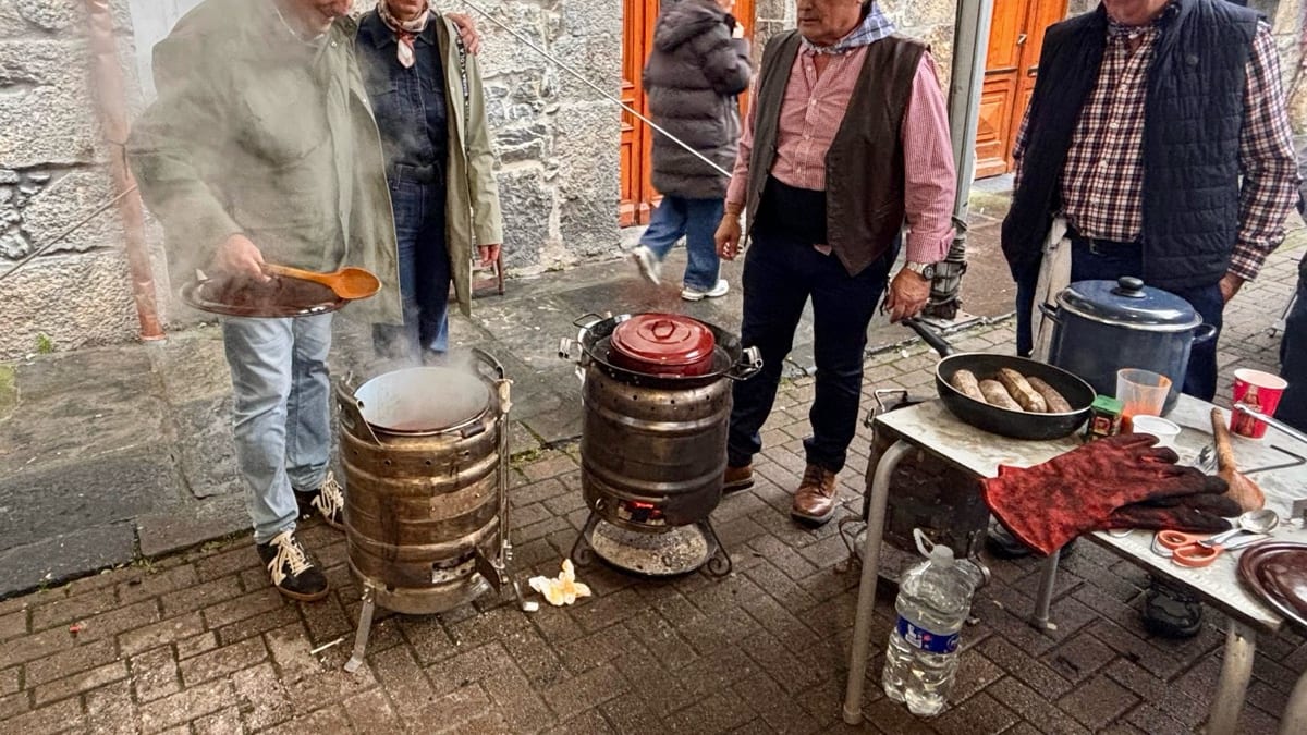 Escena de la tradicional Magosta en Ramales de la Victoria con participantes alrededor de calderos en una calle empedrada con edificios de piedra