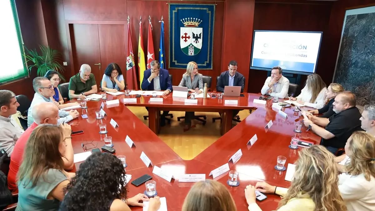 Reunión de directores de colegios públicos de Alcobendas en sala de conferencias con mesa en forma de U y banderas regionales
