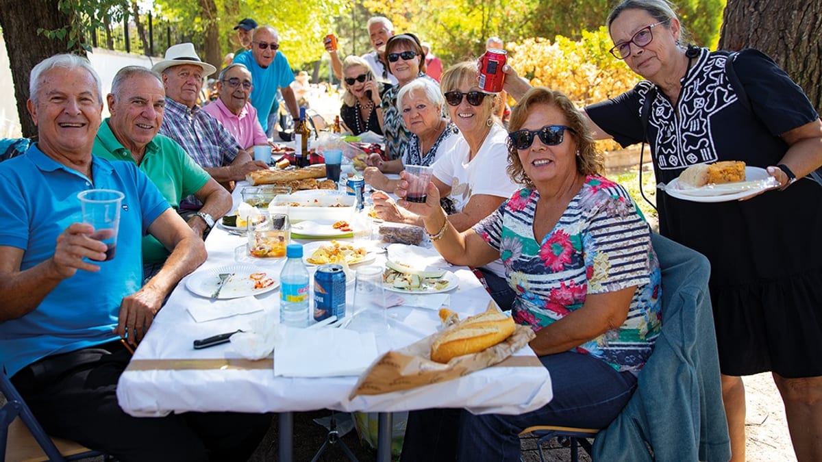 Grupo de personas adultas disfrutando de una comida al aire libre bajo los árboles en el parque de San Isidro de Rivas Vaciamadrid
